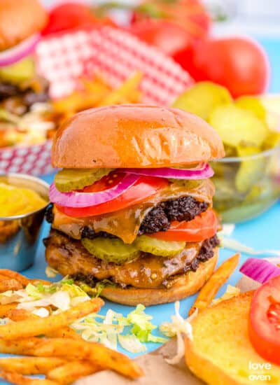 A smash burger surrounded by toppings and french fries.