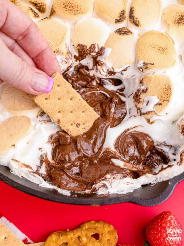 a hand dipping a graham cracker into smores dip