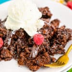 A serving of chocolate crock pot cake on a plate topped with ice cream.