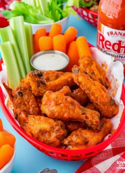 buffalo wings in a red basket with dressing, celery, carrots and a bottle of hot sauce