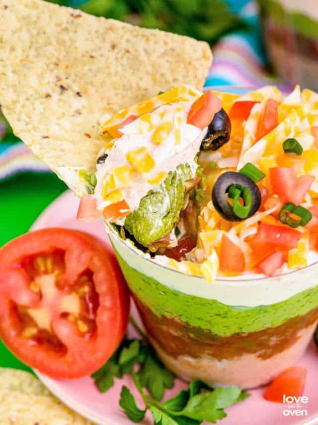 a tortilla chip scooping the contents out of the 7 layer taco dip