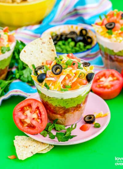 A cup of 7 layer taco dip with a tortilla chip in it.