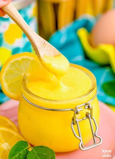 a jar of lemon curd with a spoon taking some out.