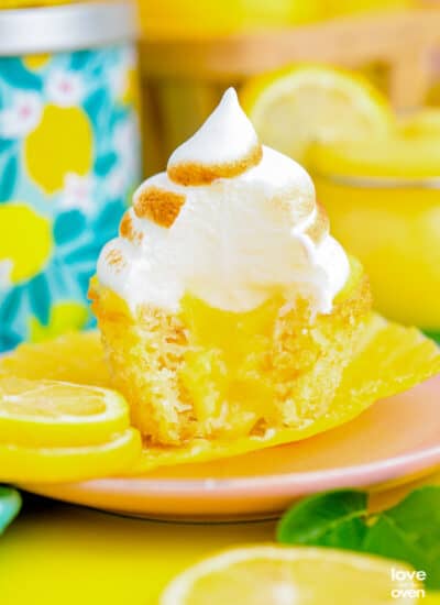 A lemon cupcake, filled with lemon curd and topped with lemon meringue, sitting on a pink plate.