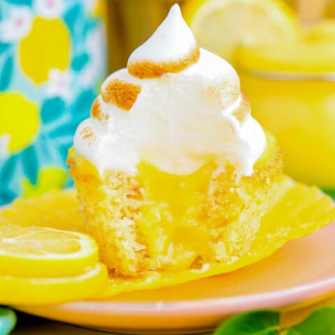 A lemon cupcake, filled with lemon curd and topped with lemon meringue, sitting on a pink plate.