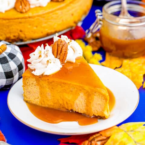 A slice of pumpkin cheesecake on a plate, surrounded by decorative fall items.
