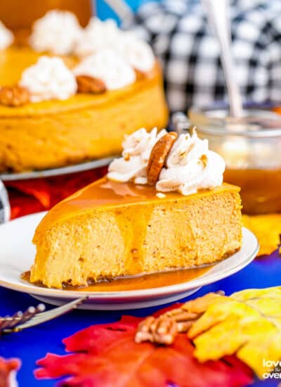 A slice of pumpkin cheesecake on a blue table with colorful fall decor.