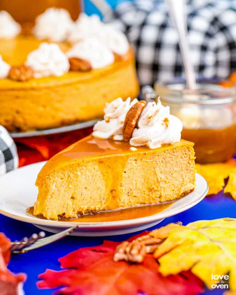 A slice of pumpkin cheesecake on a blue table with colorful fall decor.