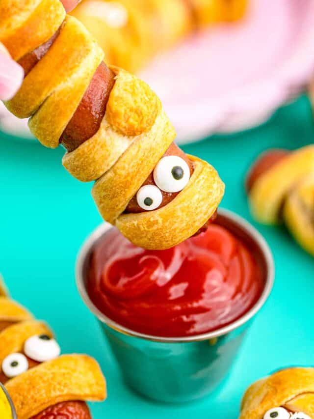 a mummy hotdog being dipped in ketchup