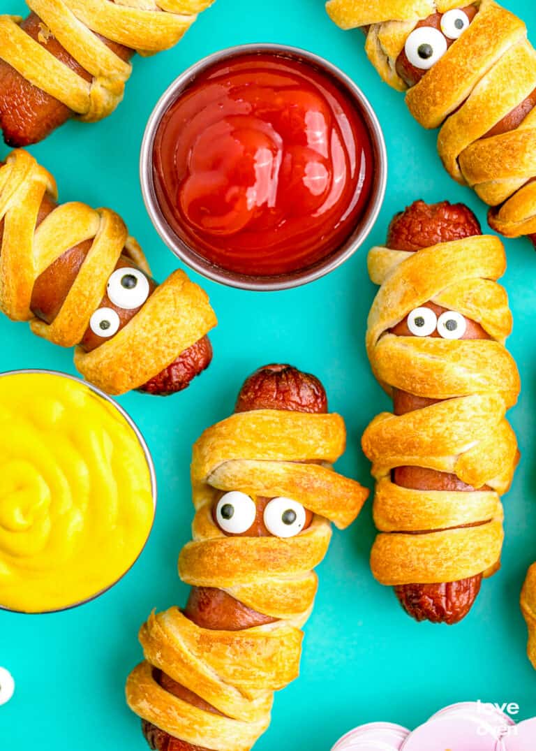 Mummy hot dogs with ketchup and mustard on a blue background.