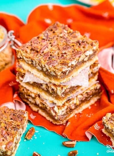 A stack of pecan pie bars on an orange napkin sitting on a blue background.