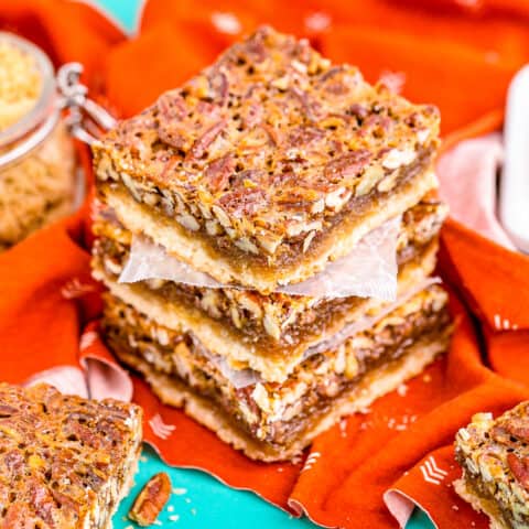 A stack of pecan pie bars on an orange napkin sitting on a blue background.