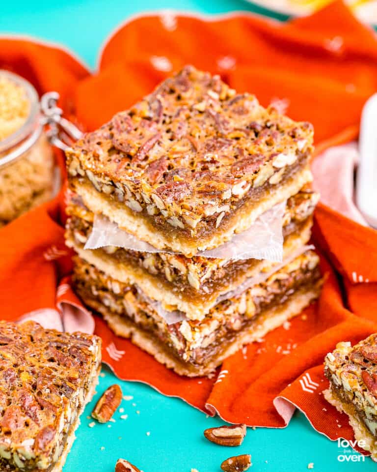 A stack of pecan pie bars on an orange napkin sitting on a blue background.