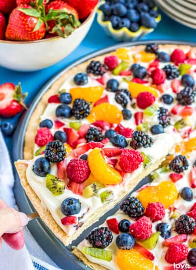 A slice of sugar cookie fruit pizza being lifted out of a pan.