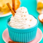 Cinnamon whipped cream with cinnamon sticks, in a blue bowl.