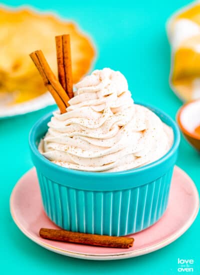 Cinnamon whipped cream with cinnamon sticks, in a blue bowl.