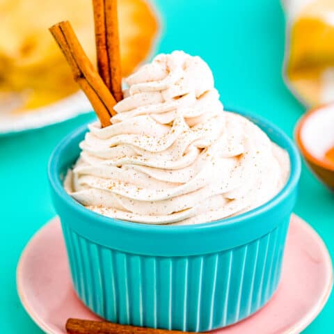 Cinnamon whipped cream with cinnamon sticks, in a blue bowl.