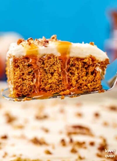A pumpkin poke cake with caramel dripping down it, on a serving spatula.