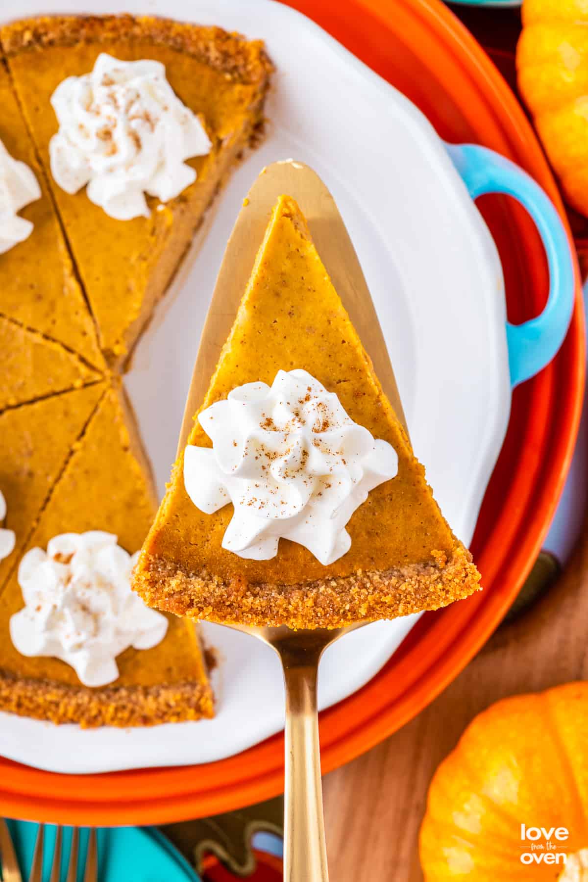 A slice of a pumpkin pie with a graham cracker crust, being served.