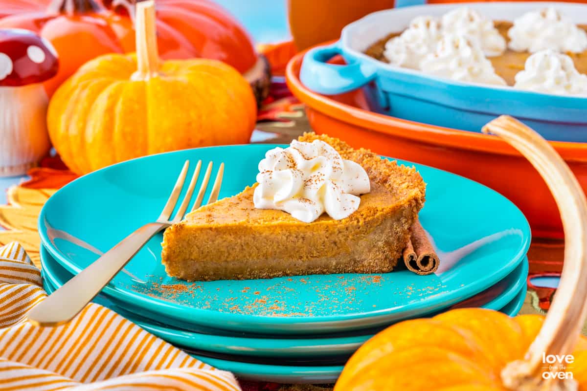 A slice of pumpkin pie with a graham cracker crust on a stack of blue plates.