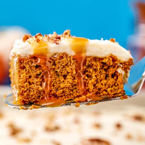 A pumpkin poke cake with caramel dripping down it, on a serving spatula.