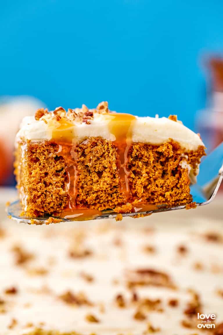 A pumpkin poke cake with caramel dripping down it, on a serving spatula.