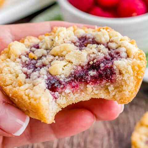 A hand holding a raspberry crumble cookie with a bite taken out.