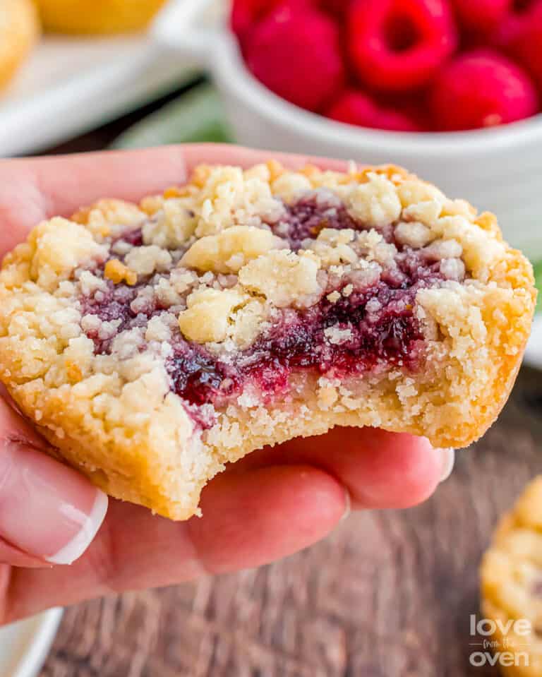 A hand holding a raspberry crumble cookie with a bite taken out.