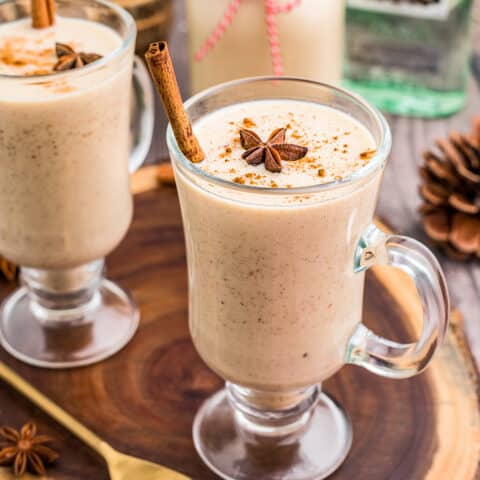 Two glasses of Coquito on a wooden slab.