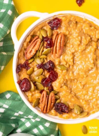 A bowl of pumpkin oatmeal topped with nuts, cranberries and seeds.