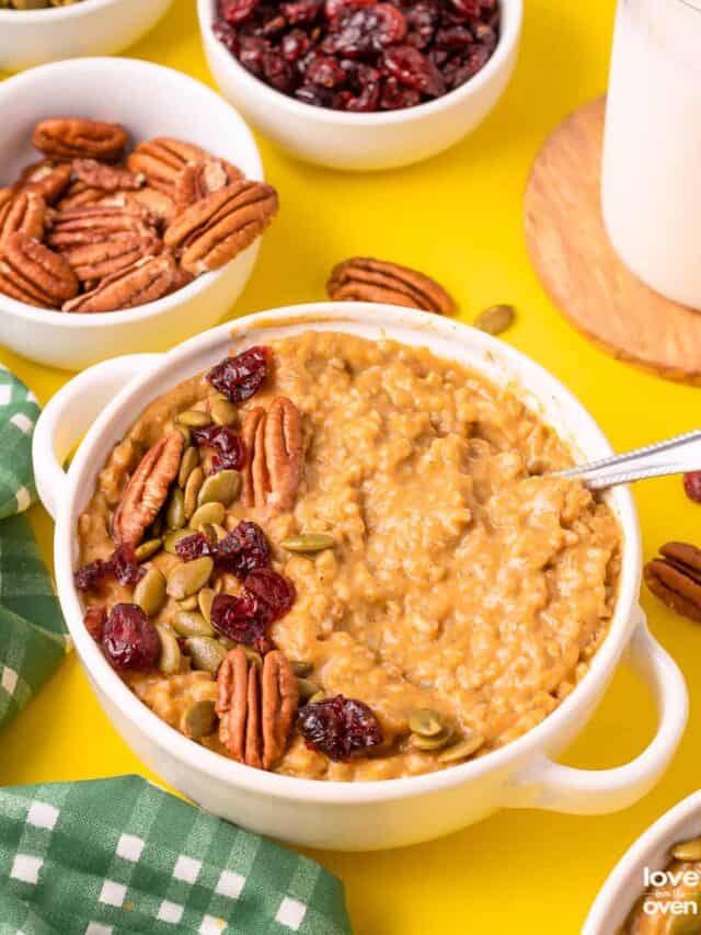 A bowl of pumpkin oatmeal topped with nuts, cranberries and seeds.