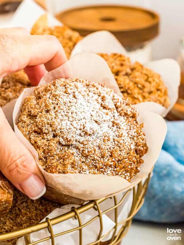 A hand grabbing a pumpkin streusel muffin from a basket.