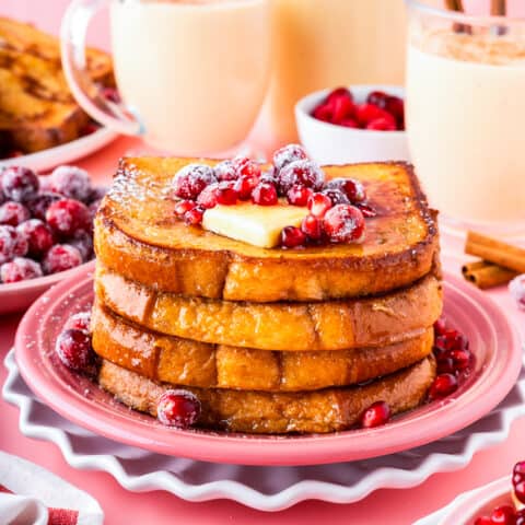 a stack of eggnog french toast with butter, berries and syrup on a pink plate