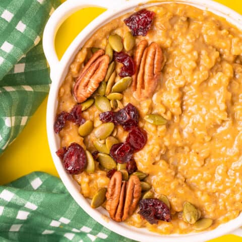 A bowl of pumpkin oatmeal topped with nuts, cranberries and seeds.