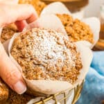 A hand grabbing a pumpkin streusel muffin from a basket.