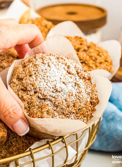 A hand grabbing a pumpkin streusel muffin from a basket.