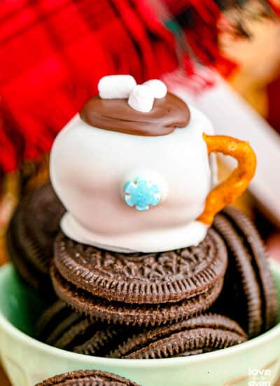 An oreo truffle, that looks like a mug of hot cocoa, on top of a bowl of Oreos.