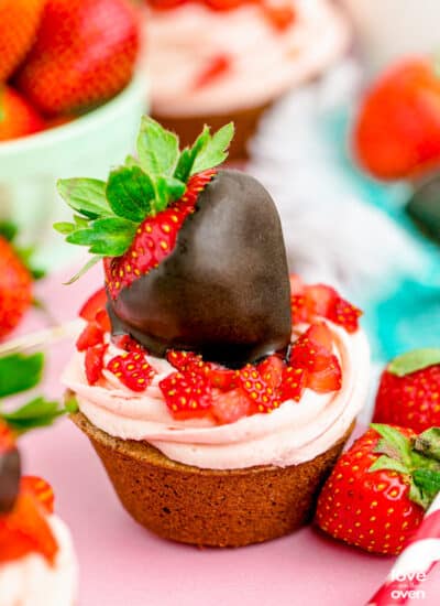 A chocolate cupcake with strawberry frosting and a chocolate covered strawberry on top.