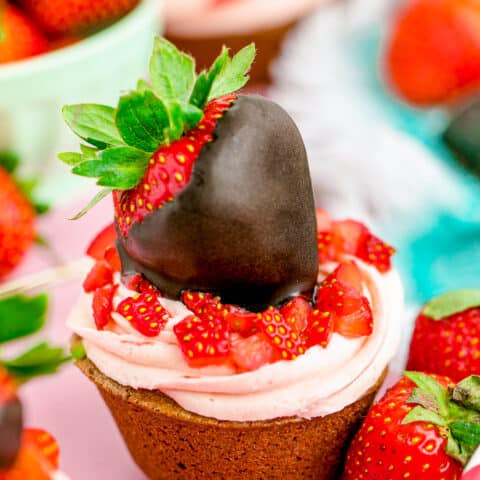A chocolate cupcake with strawberry frosting and a chocolate covered strawberry on top.