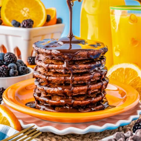 A stack of chocolate pancakes with chocolate sauce being poured over the top.