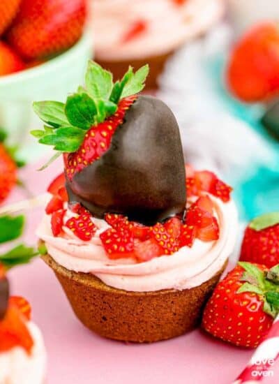 A chocolate cupcake with strawberry frosting and a chocolate covered strawberry on top.