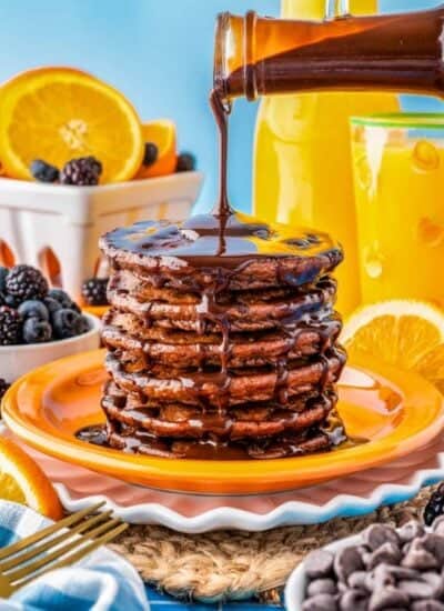 A stack of chocolate pancakes with chocolate sauce being poured over the top.