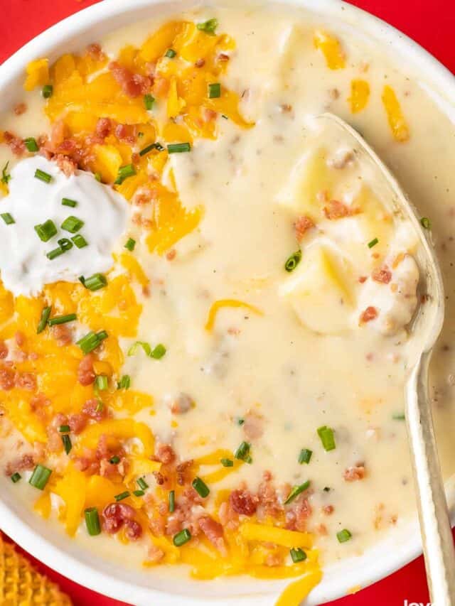 A bowl of sausage and potato soup topped with cheese, bacon and sour cream.