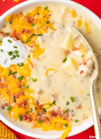 A bowl of sausage and potato soup topped with cheese, bacon and sour cream.