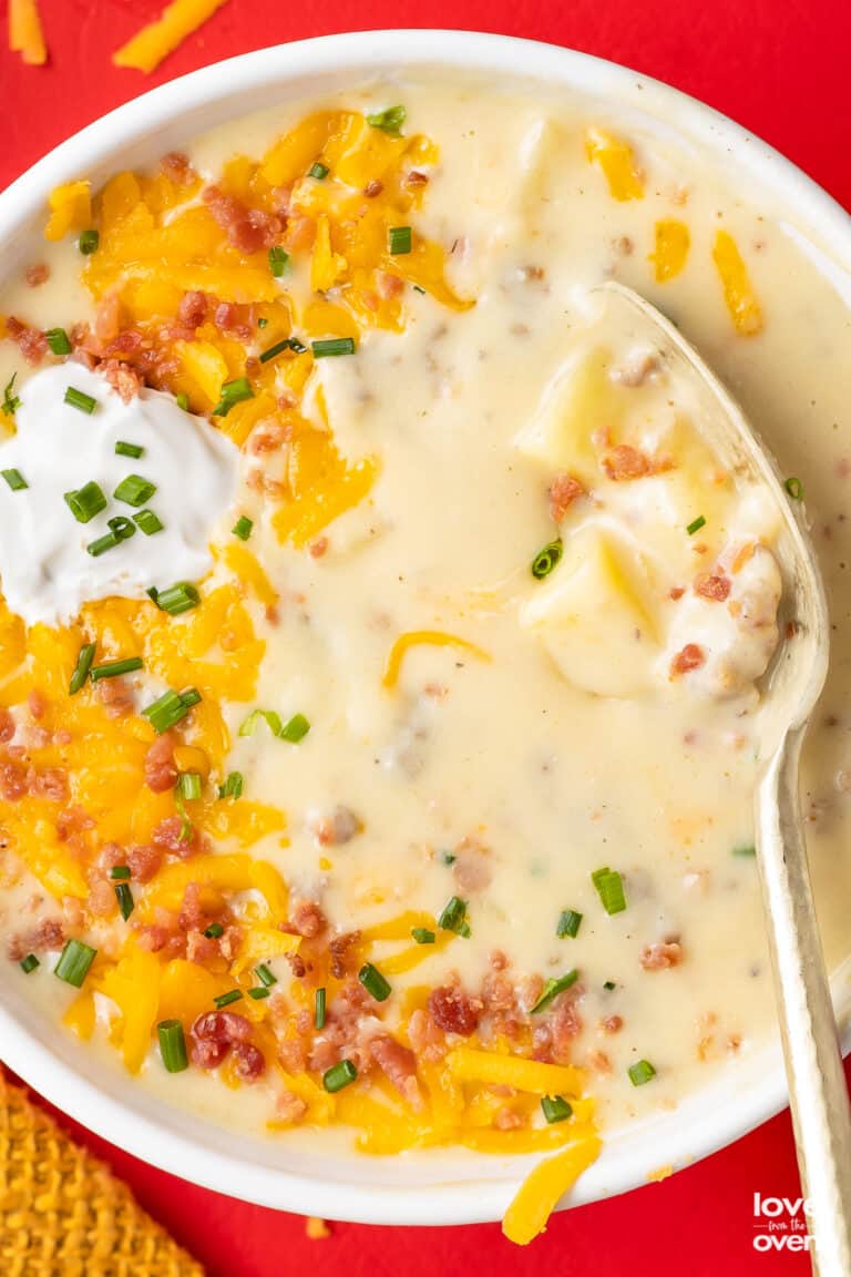 A bowl of sausage and potato soup topped with cheese, bacon and sour cream.