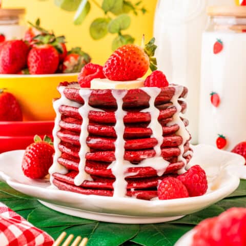 a stack of red velvet pancakes with cream cheese syrup topped with berries