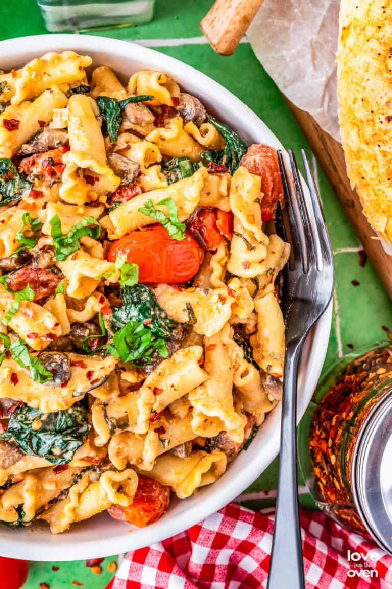A bowl of Boursin cheese pasta on a green background.