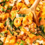 A wooden spoon stirring Sausage Tortellini Soup