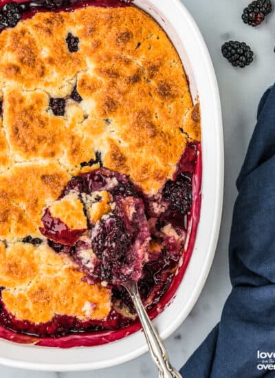 A spoon taking a serving of blackberry cobbler out of a baking dish.