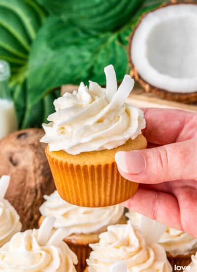 A hand holding a coconut cupcake with a green background.